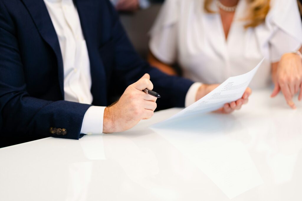 Deux personnes relisent un document sur une table blanche, stylo à la main.