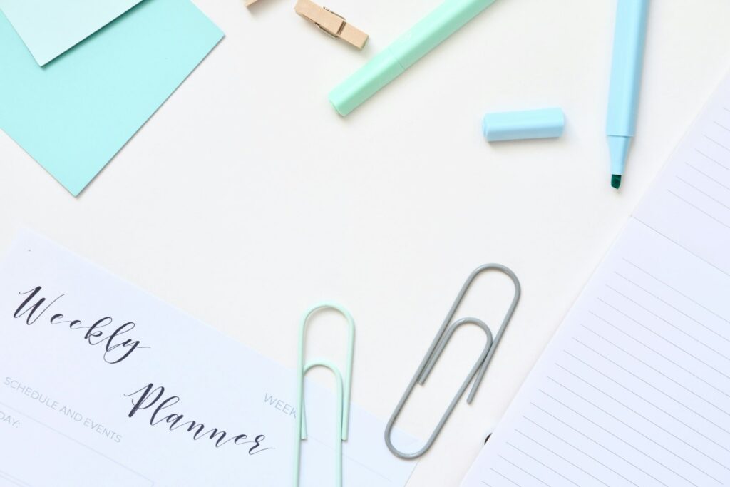 Agenda hebdomadaire et fournitures pastel sur une surface blanche.