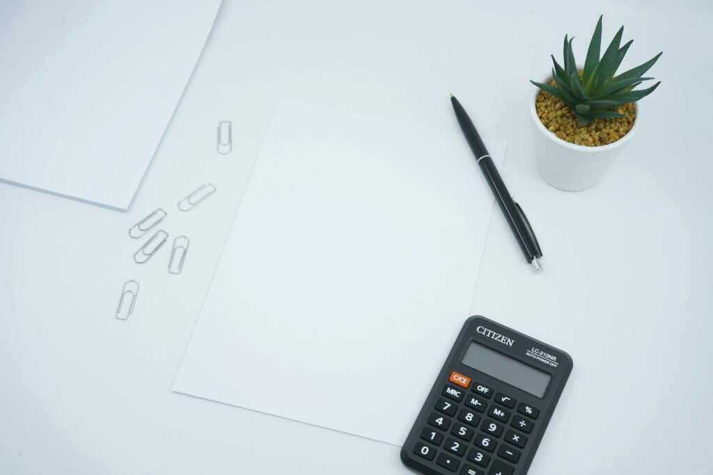 Calculatrice, stylo et feuilles de papier sur un bureau blanc.