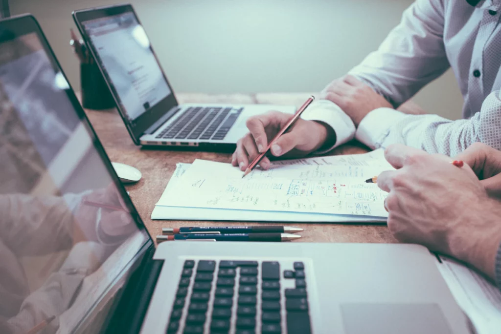 Deux personnes examinent et annotent des documents sur une table de travail.