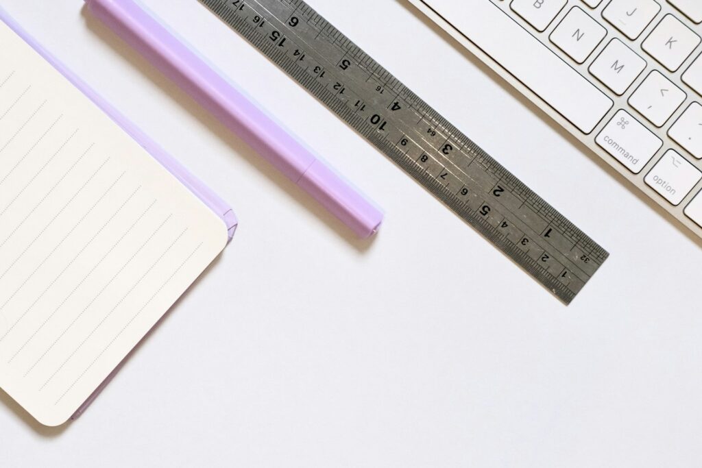 Règle métallique, carnet et clavier sur un bureau blanc.