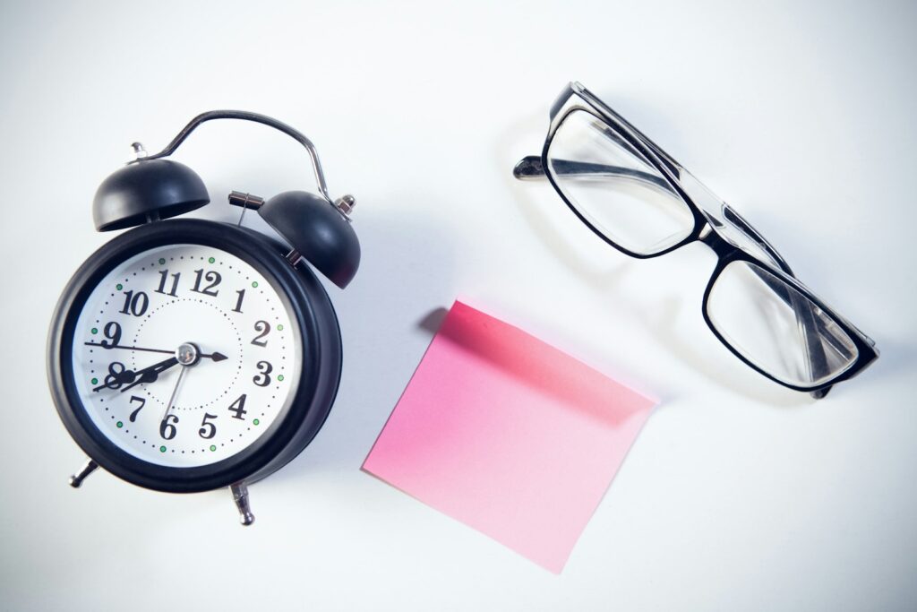 Réveil, lunettes et note rose sur une surface blanche.