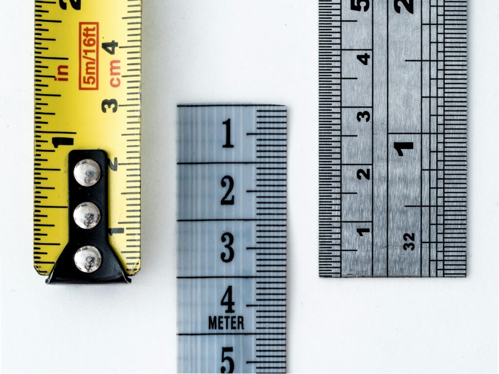 Plusieurs règles et rubans de mesure alignés sur un fond blanc.