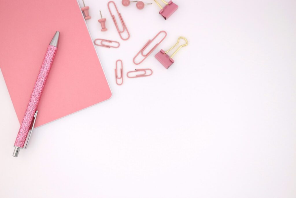 Carnet rose, stylo et attaches de bureau sur un fond blanc.