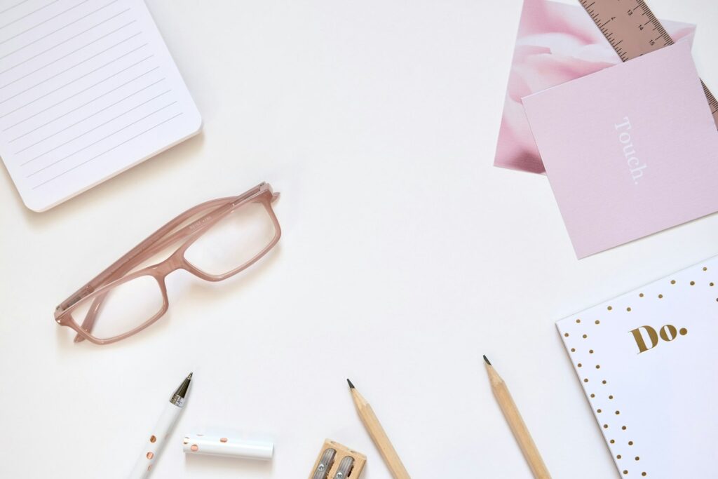 Lunettes, carnets et crayons disposés sur un bureau blanc.