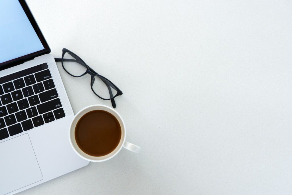 Ordinateur portable, lunettes et tasse posés sur un bureau blanc.