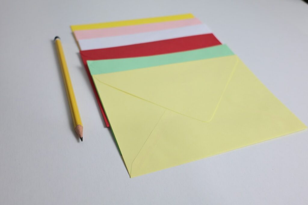 Enveloppes colorées et crayon sur une surface blanche.
