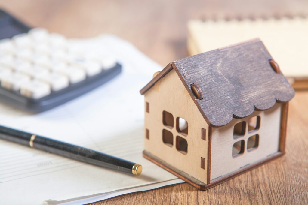 Maquette de maison, crayon et documents sur une table claire.