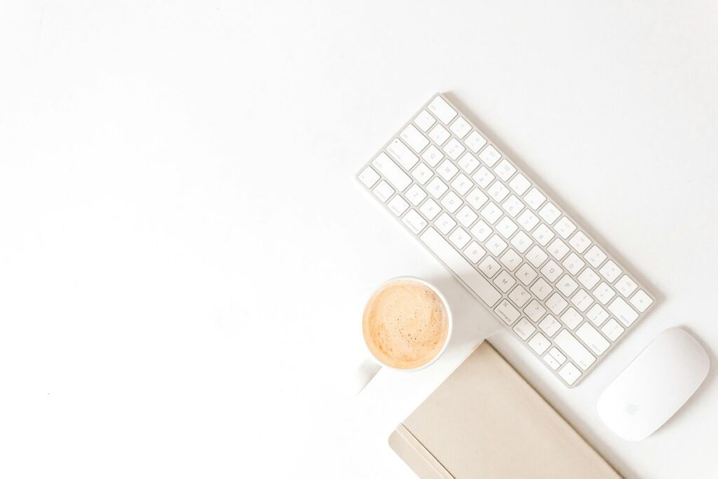 Clavier, souris et tasse disposés sur un bureau blanc.
