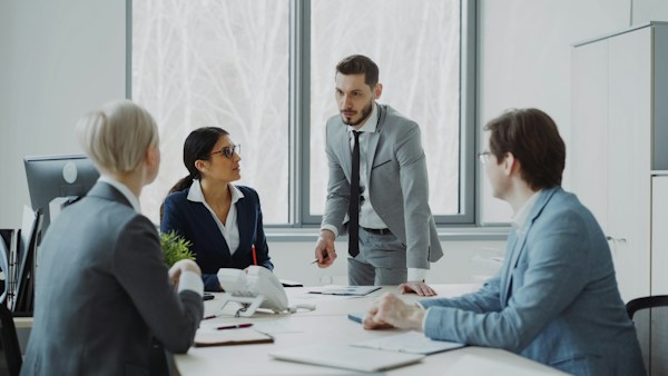 Quatre collègues échangent autour de documents sur une table dans un bureau clair.