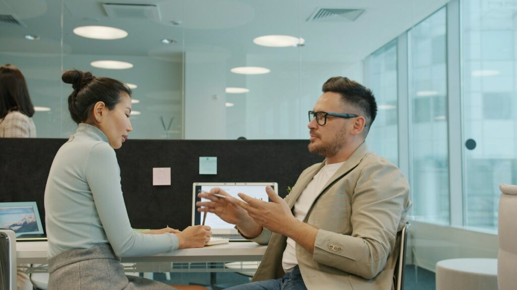 Deux professionnels échangent à une table blanche dans un bureau clair.