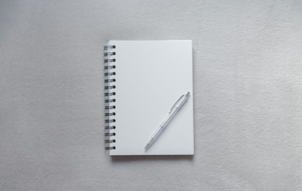 Carnet blanc à spirales et stylo clair sur une surface gris clair.