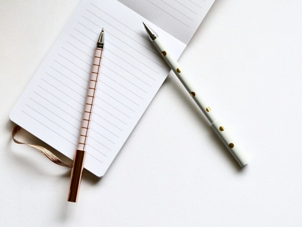 Deux stylos fins et bloc de papier blanc à lignes sur un fond clair.