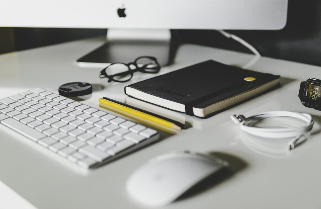 Écran, dossiers et fournitures sur un bureau blanc.
