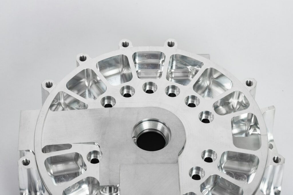 Pièce métallique circulaire usinée, avec perçages et évidements, sur fond clair.