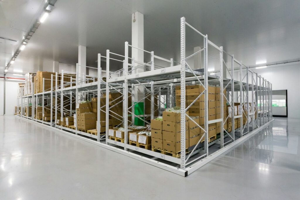 Rayonnages métalliques et cartons dans un local logistique blanc et lumineux.