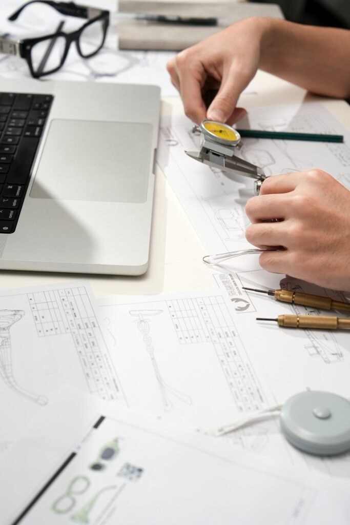 Mains utilisant un pied à coulisse au-dessus de dessins techniques sur une table blanche.