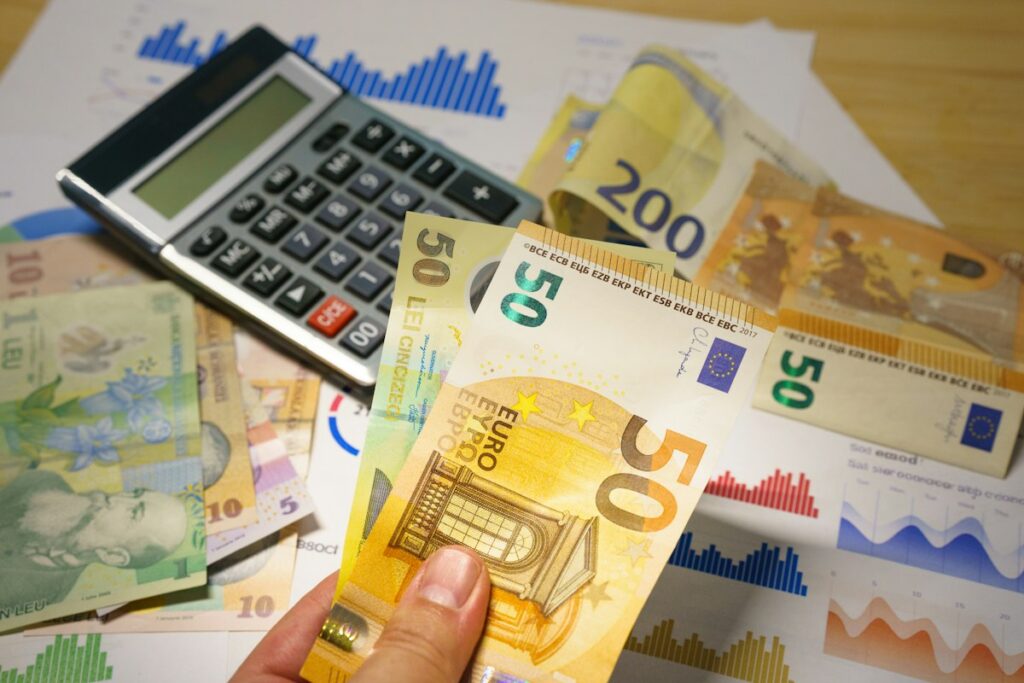 Personne tenant des billets en euros près d’une calculatrice et de graphiques.