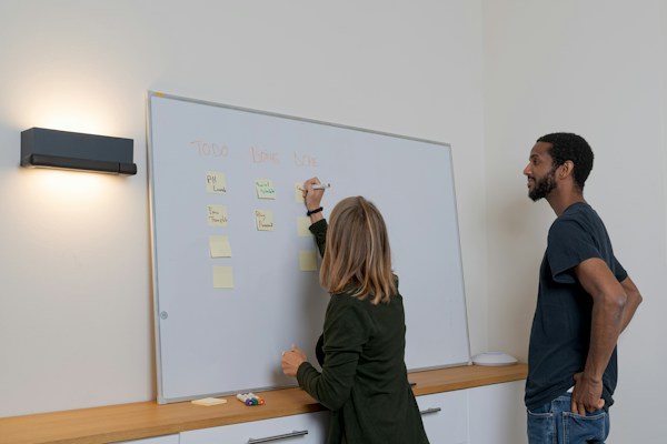 Deux personnes échangent devant un tableau blanc et des notes adhésives.