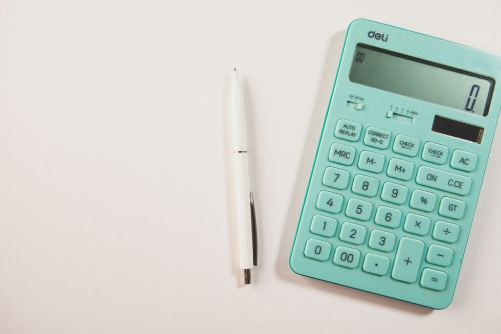 Calculatrice turquoise et stylo blanc sur une surface claire.