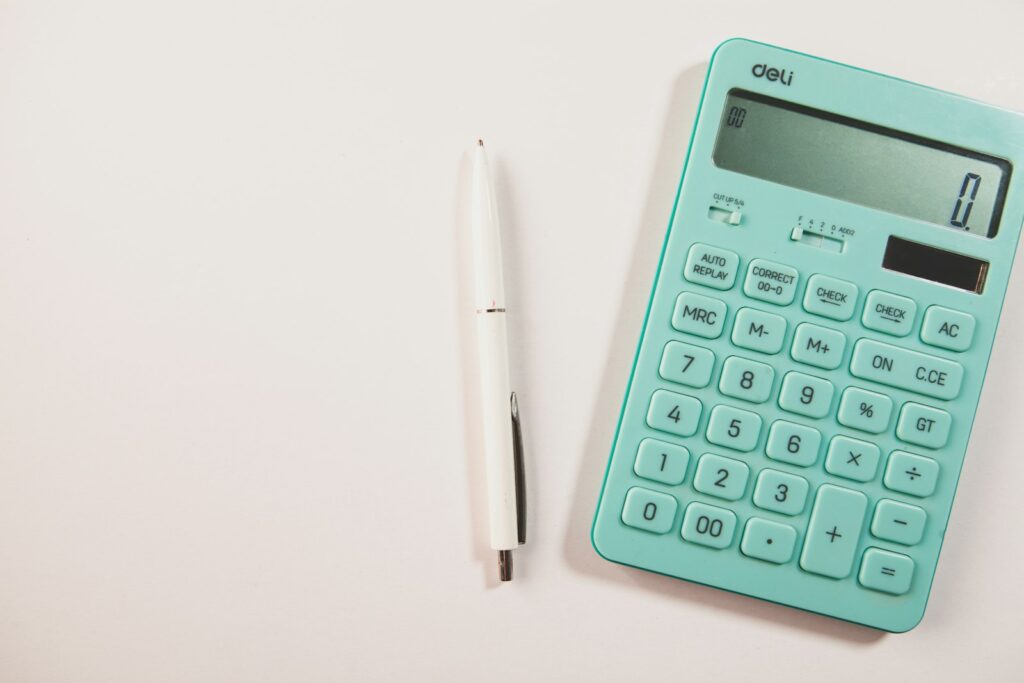 Calculatrice turquoise et stylo blanc sur une surface claire.