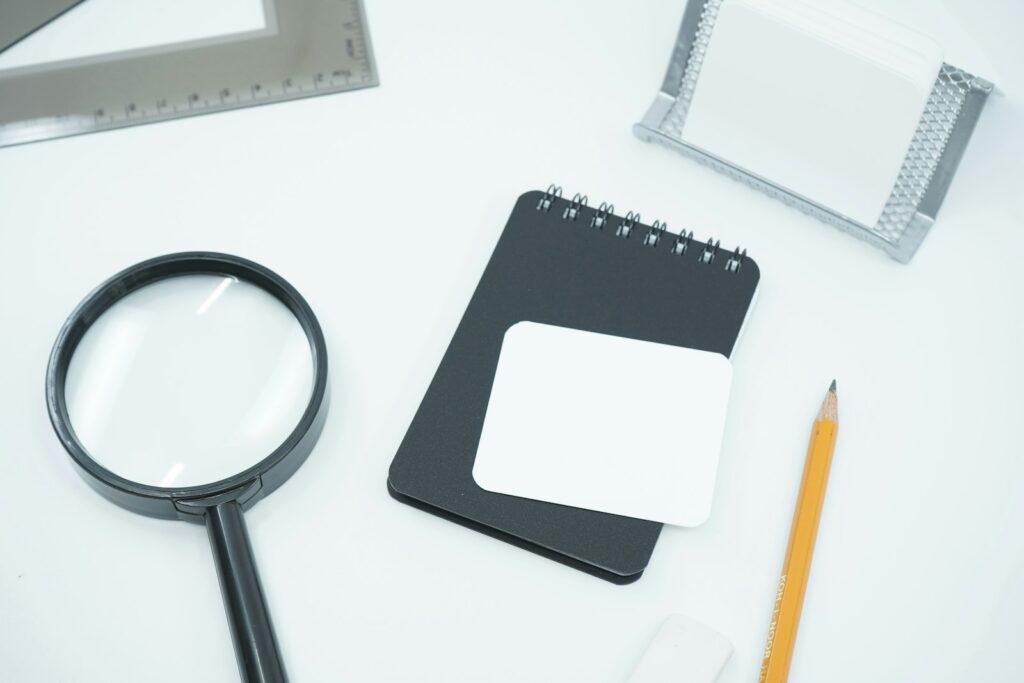 Loupe, carnet, crayon et fiches disposés sur un bureau blanc.